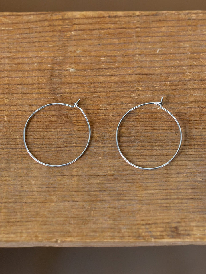 The Levy Gold/Silver Hoop Earrings by Savannah Sevens western life{&}style, known for being hypoallergenic and tarnish resistant, are displayed side by side on a wooden surface.