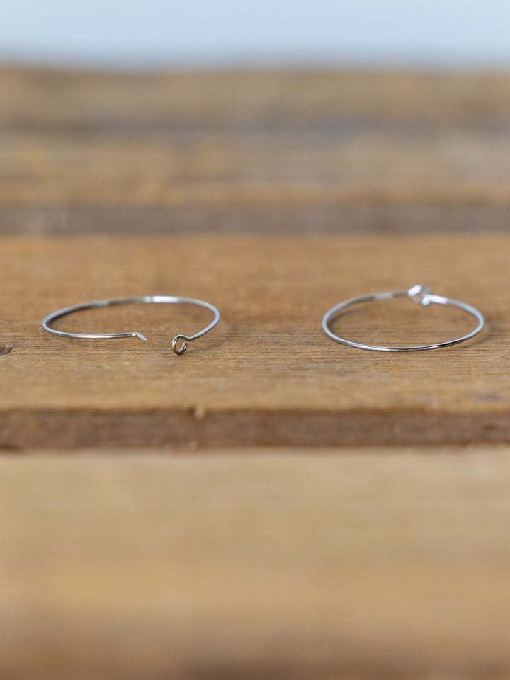 Two thin Levy Gold/Silver Hoop Earrings by Savannah Sevens western life{&}style rest on a wooden surface, with one hoop open and the other closed. Both are tarnish resistant.