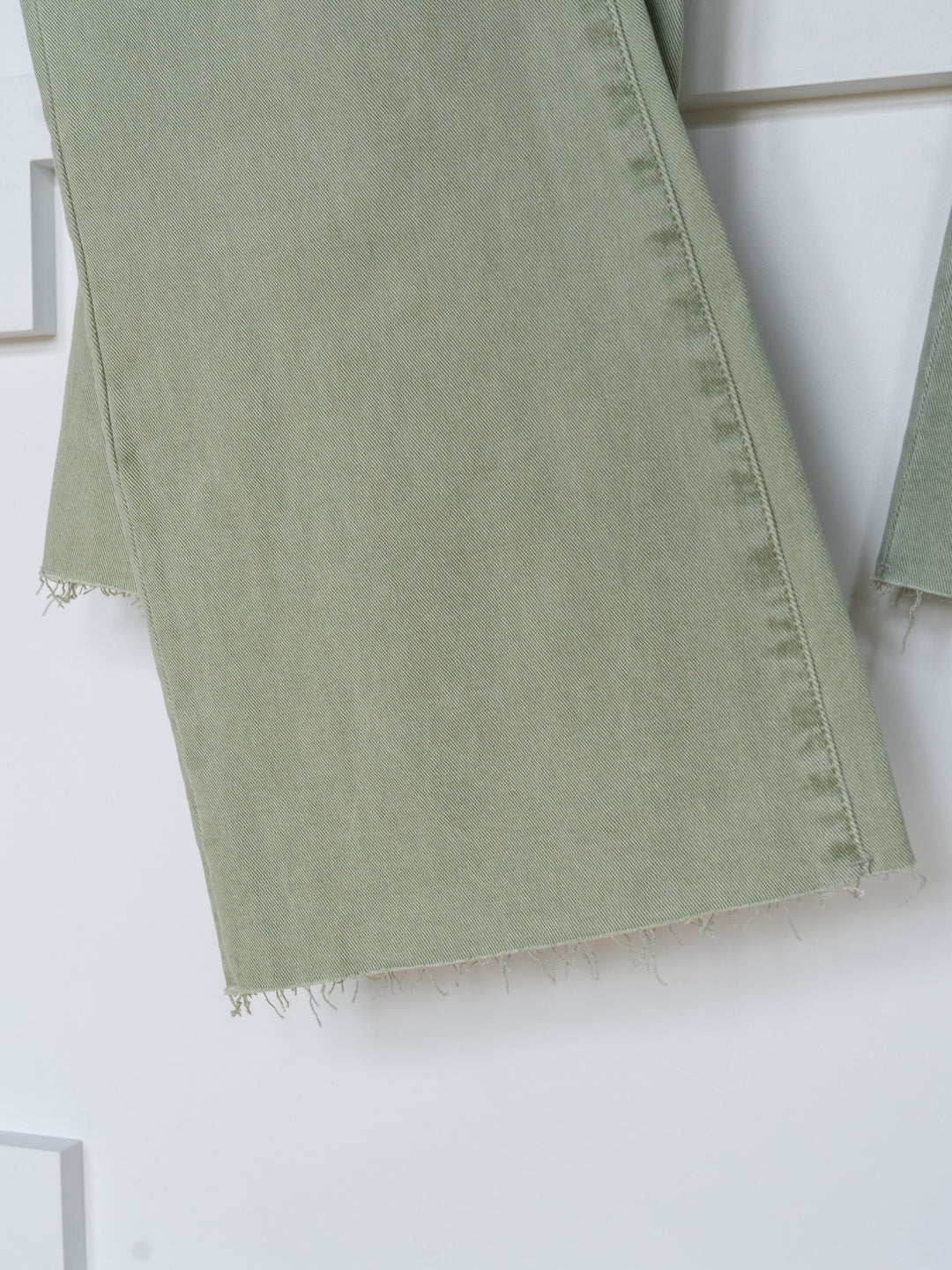 Close-up of The Lindy High Rise Wide Leg Jean by Savannah Sevens western life{&}style, featuring sage denim pant legs with a raw cut hem, hanging against a white background.