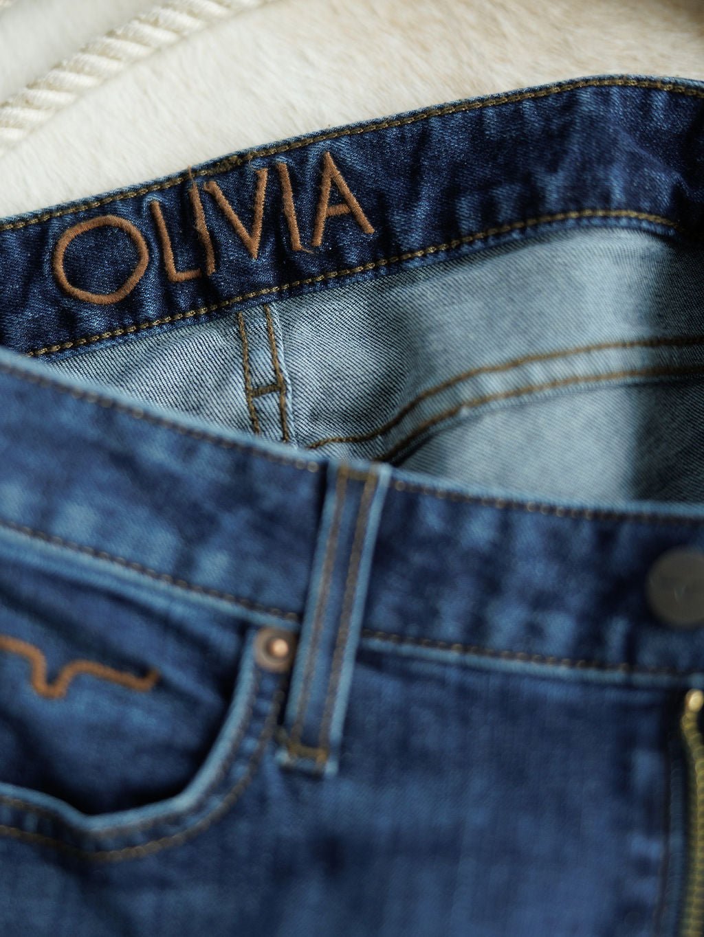 Close-up of The Livy High Rise 90's Wide Leg Jean *Exclusive* by Savannah Sevens western life{&}style, featuring premium blue denim with visible stitching, pocket detailing, and "OLIVIA" stitched in brown on the inside waistband.