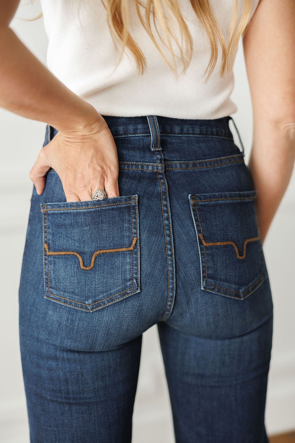 A woman with long, wavy hair wears The Livy High Rise 90's Wide Leg Jean *Exclusive* by Savannah Sevens western life{&}style, featuring premium denim and decorative back pocket stitching, with one hand in her pocket.