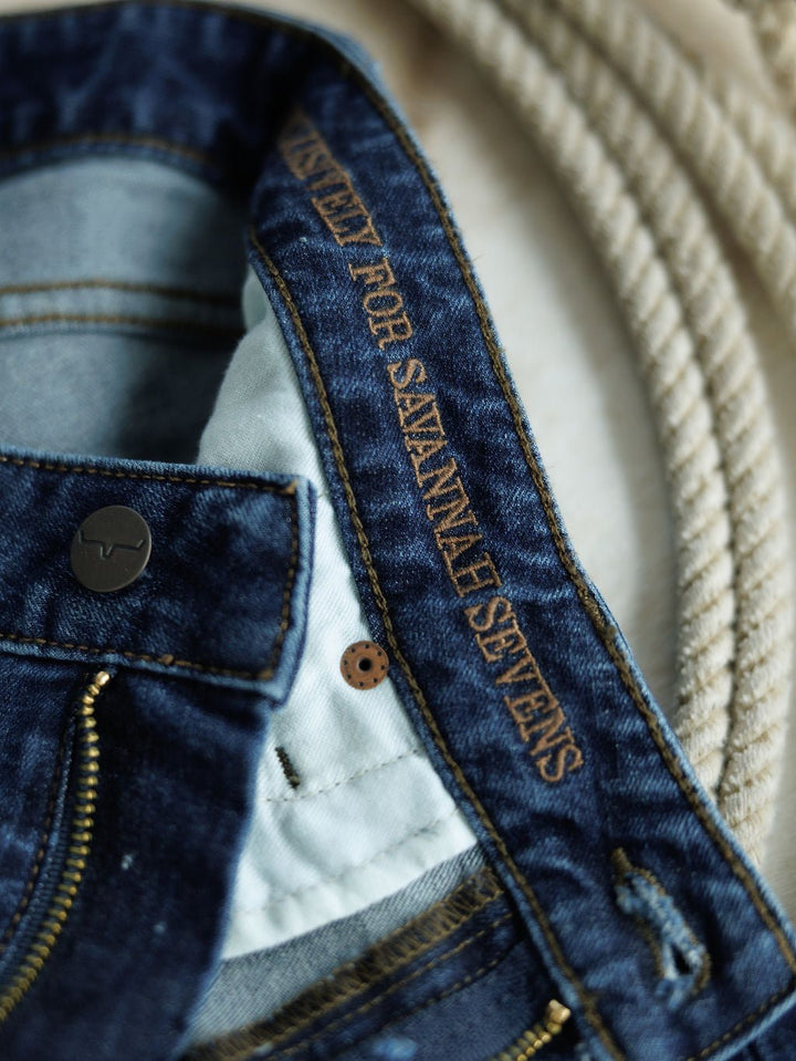 Close-up of The Livy High Rise 90's Wide Leg Jean *Exclusive* by Savannah Sevens western life{&}style, featuring "EXCLUSIVELY FOR SAVANNAH SEVENS" stitched on the inner waistband. Classic blue premium denim with a coiled rope in the background.