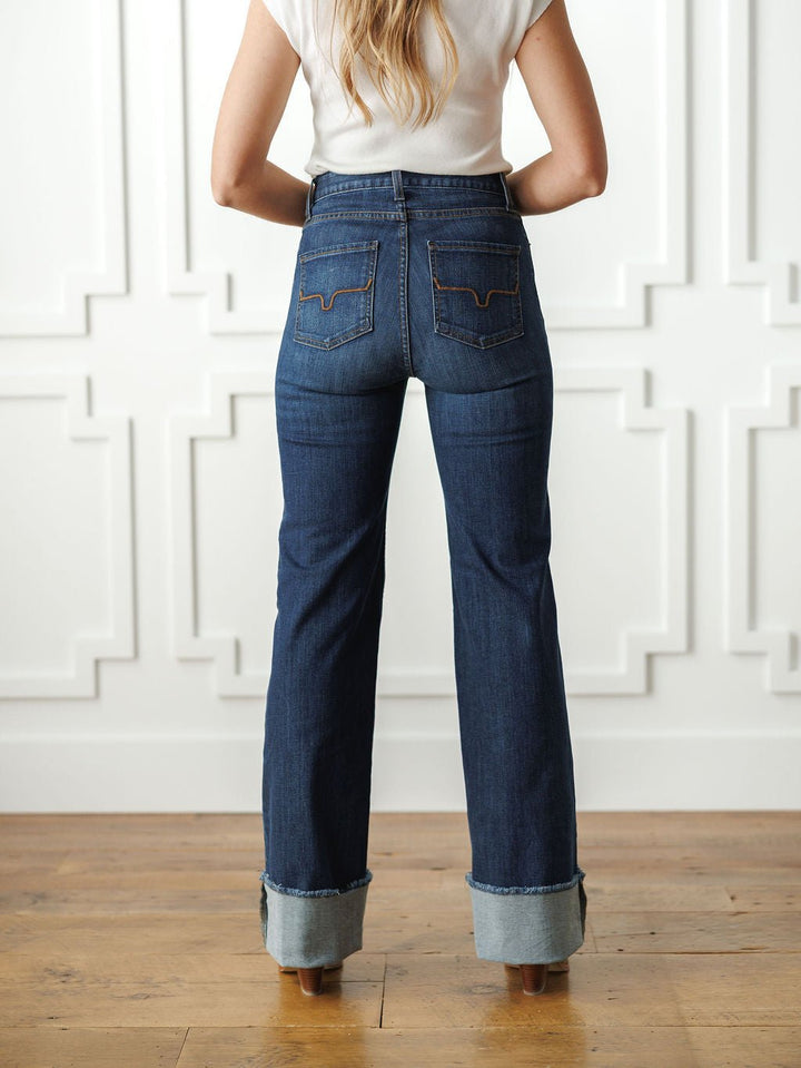 A woman stands indoors on a wooden floor by a white paneled wall, wearing Savannah Sevens western life{&}style's The Livy High Rise 90's Wide Leg Jean *Exclusive* and a white short-sleeve top.