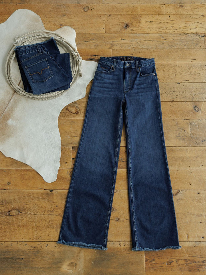 Two pairs of The Livy High Rise 90's Wide Leg Jean by Savannah Sevens western life{&}style in dark blue are shown on a wooden floor—one folded on a cowhide rug, the other laid flat with frayed hems.