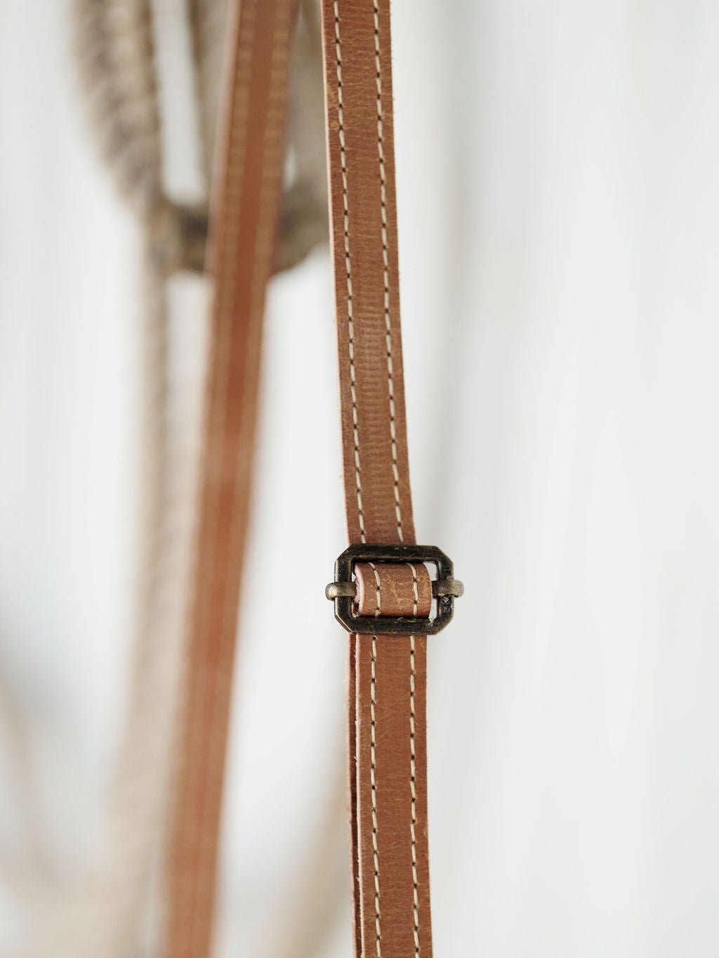 Close-up of the Lomita Leather Crossbody Bag by Savannah Sevens western life{&}style, highlighting its adjustable brown leather strap with white stitching and a small metal buckle against a blurred light background.
