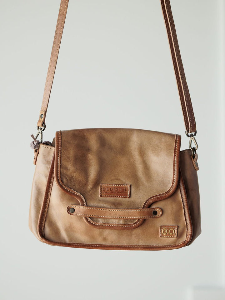 The Lomita Leather Crossbody Bag by Savannah Sevens western life{&}style, featuring a flap closure, decorative stitching, and adjustable strap, hangs against a light, neutral background.