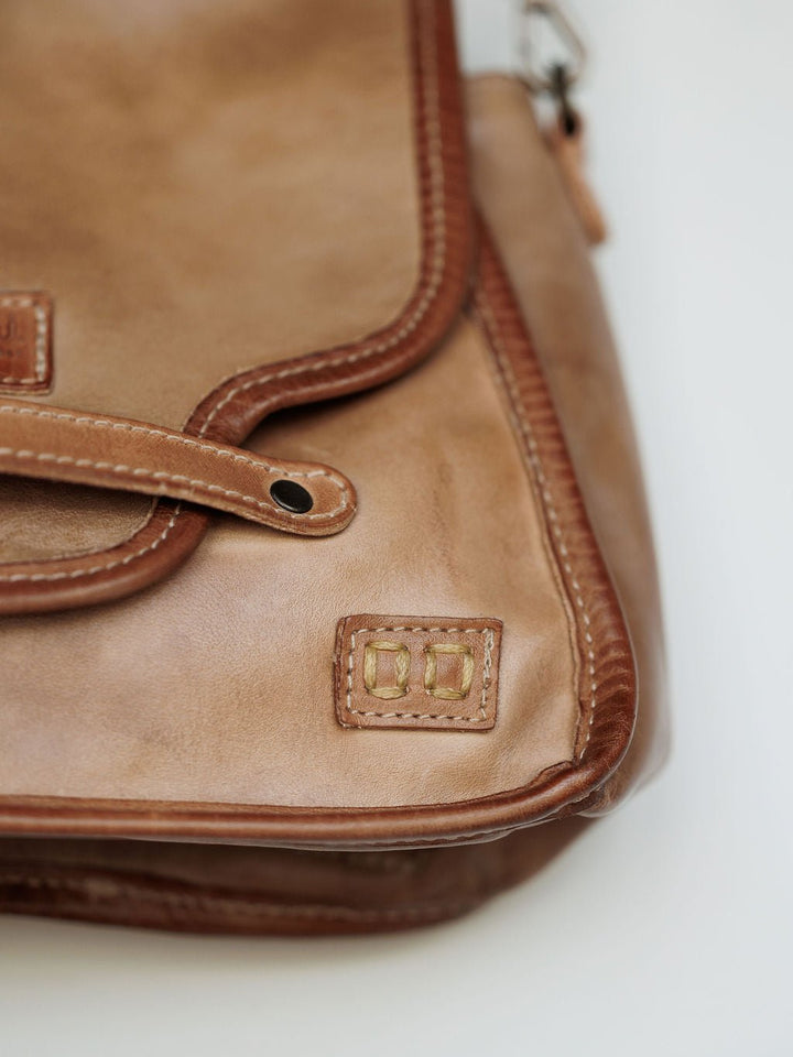 A close-up of the Lomita Leather Crossbody Bag by Savannah Sevens western life{&}style shows visible stitching, a decorative square patch at the bottom right, the flap, part of the handle, and an adjustable strap.