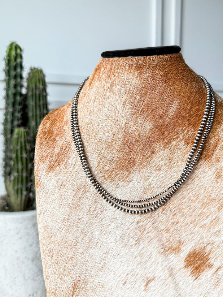 The Los Alamos Layered Navajo Pearl Necklace by Savannah Sevens western life{&}style, crafted from sterling silver, is displayed on a brown and white cowhide-covered bust with a potted cactus in the background against a white wall.