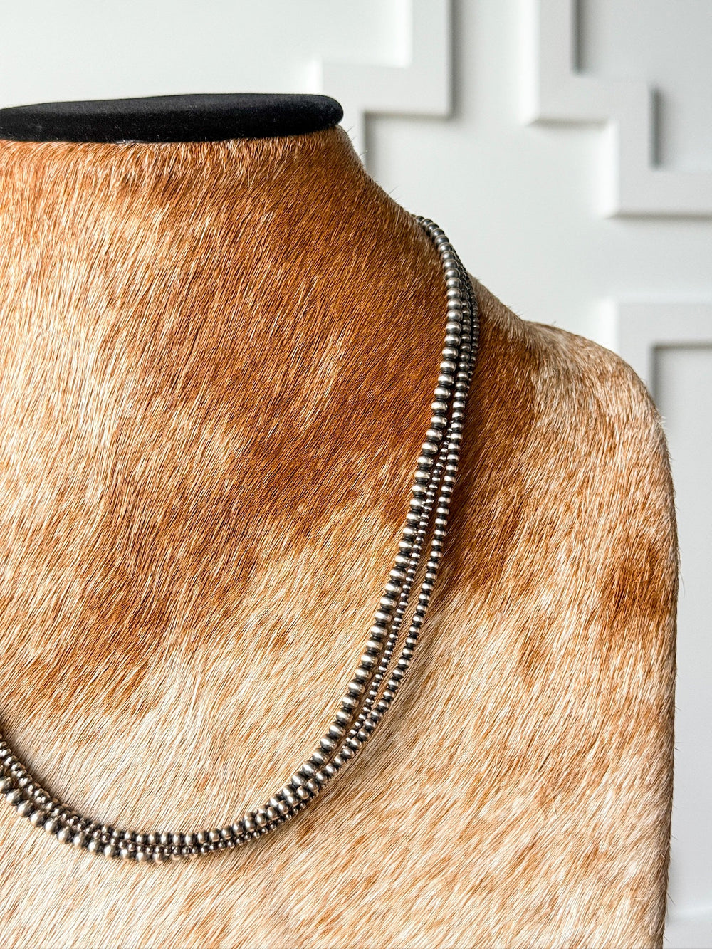 The Los Alamos Layered Navajo Pearl Necklace by Savannah Sevens western life{&}style is showcased on a brown and white cowhide-covered bust, set against a white textured wall.