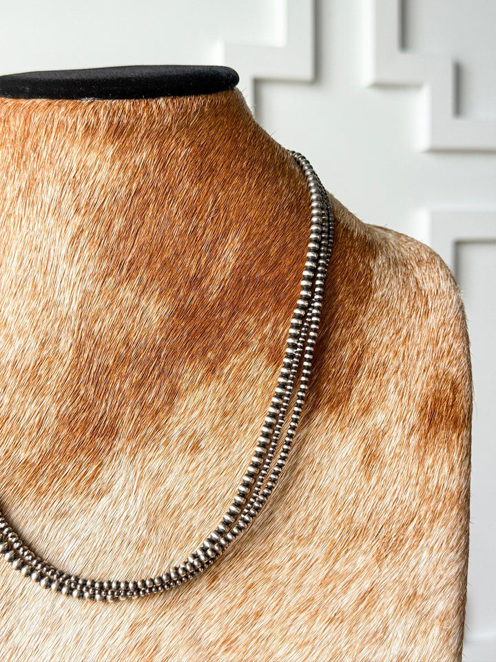 The Los Alamos Layered Navajo Pearl Necklace by Savannah Sevens western life{&}style is showcased on a brown and white cowhide-covered bust, set against a white textured wall.