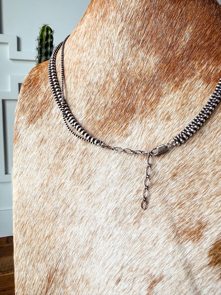 The Los Alamos Layered Navajo Pearl Necklace by Savannah Sevens western life{&}style is elegantly draped around the neck of a brown and white cowhide bust with a cactus and white wall in the background.
