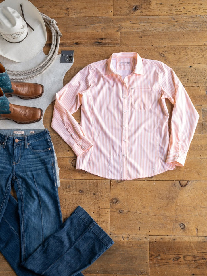 A Savannah Sevens western life{&}style The Lovilia pink and white striped sun shirt is laid out on a wooden floor beside blue jeans, brown cowboy boots, a gray tee, a white cowboy hat, and turquoise and brown western boots.