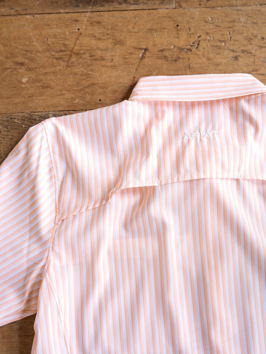 The Lovilia by Savannah Sevens western life{&}style is a light orange and white striped long sleeve shirt with a collar, featuring moisture wicking, sun protection, and "ARIAT" embroidered in white on the back shoulder.