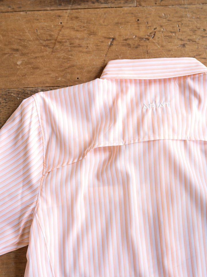 The Lovilia by Savannah Sevens western life{&}style is a light orange and white striped long sleeve shirt with a collar, featuring moisture wicking, sun protection, and "ARIAT" embroidered in white on the back shoulder.