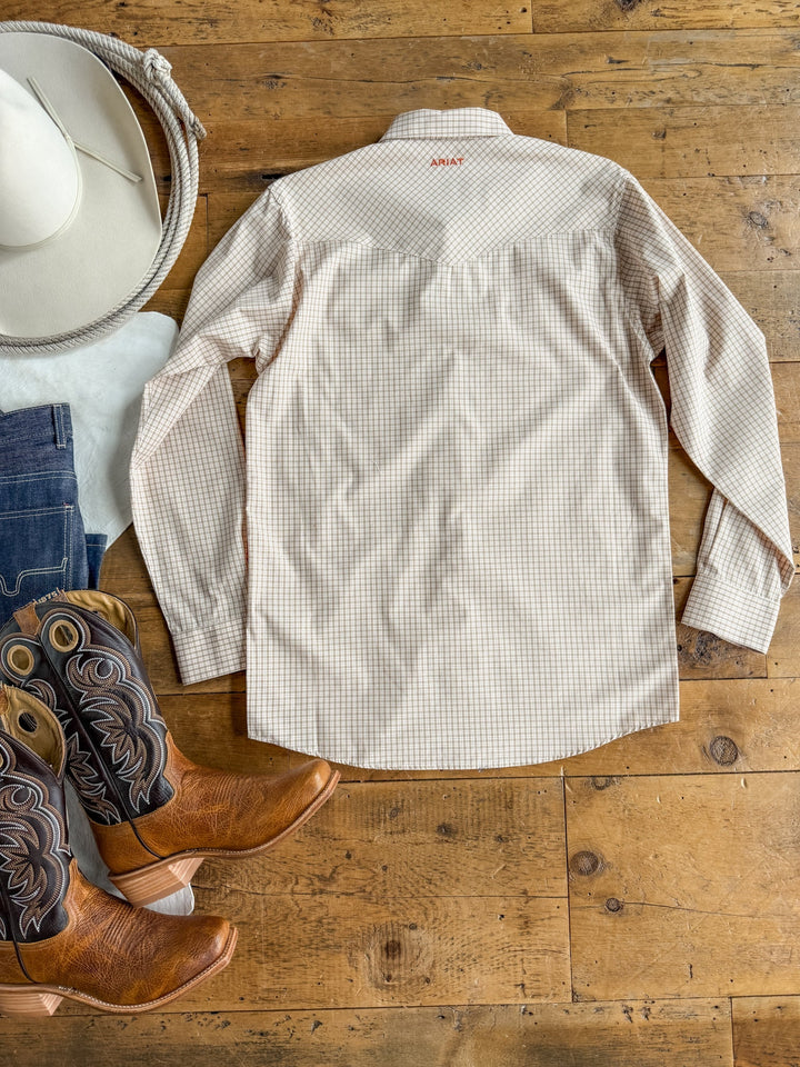 The Lyford Ariat Men’s Plaid Pearl Snap from Savannah Sevens western life{&}style is laid flat on a wooden floor alongside a white cowboy hat, dark jeans, and brown cowboy boots with black and tan stitching.