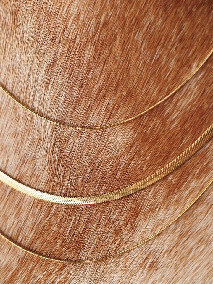 The Lynden Necklace by Savannah Sevens western life{&}style—three delicate gold layers—rests in graceful curves on light brown animal fur, highlighting its elegance against the textured background.