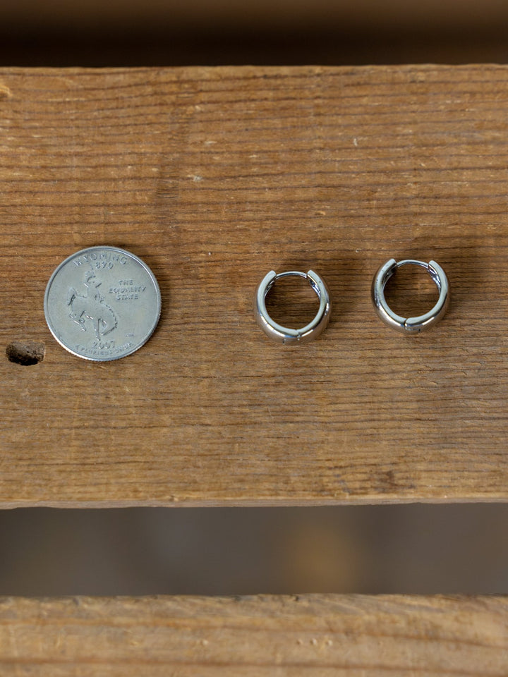 A U.S. quarter and two Madera Silver Mini Hoop Earrings by Savannah Sevens western life{&}style are shown side by side on a wooden surface, highlighting the delicate design of these earrings.