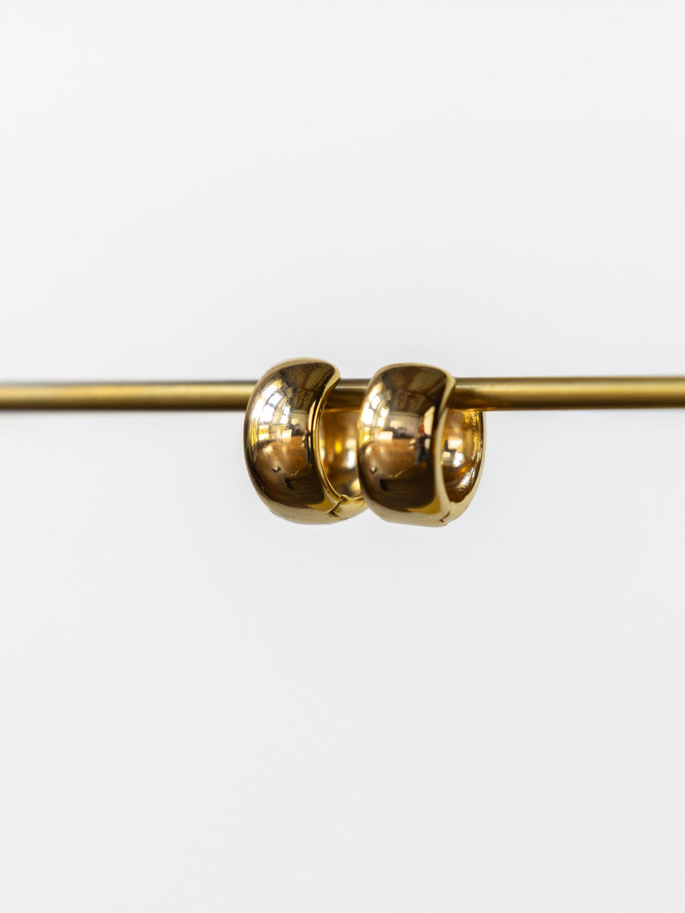 The Madera Gold/Silver Mini Hoop Earrings by Savannah Sevens western life{&}style hang side by side on a horizontal gold rod against a plain white background.