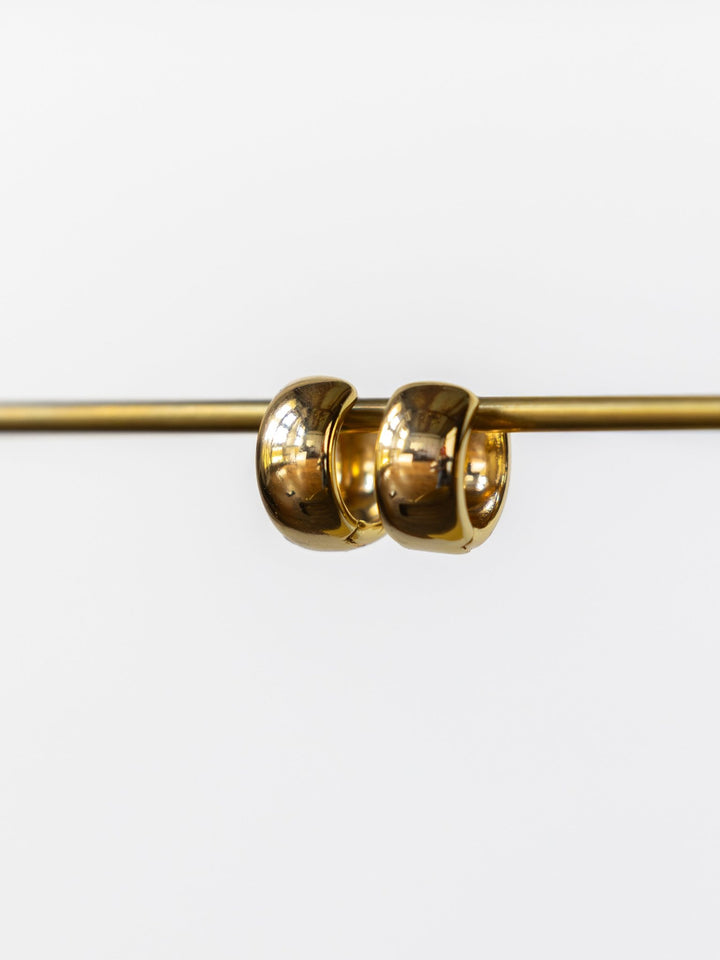 The Madera Gold/Silver Mini Hoop Earrings by Savannah Sevens western life{&}style hang side by side on a horizontal gold rod against a plain white background.