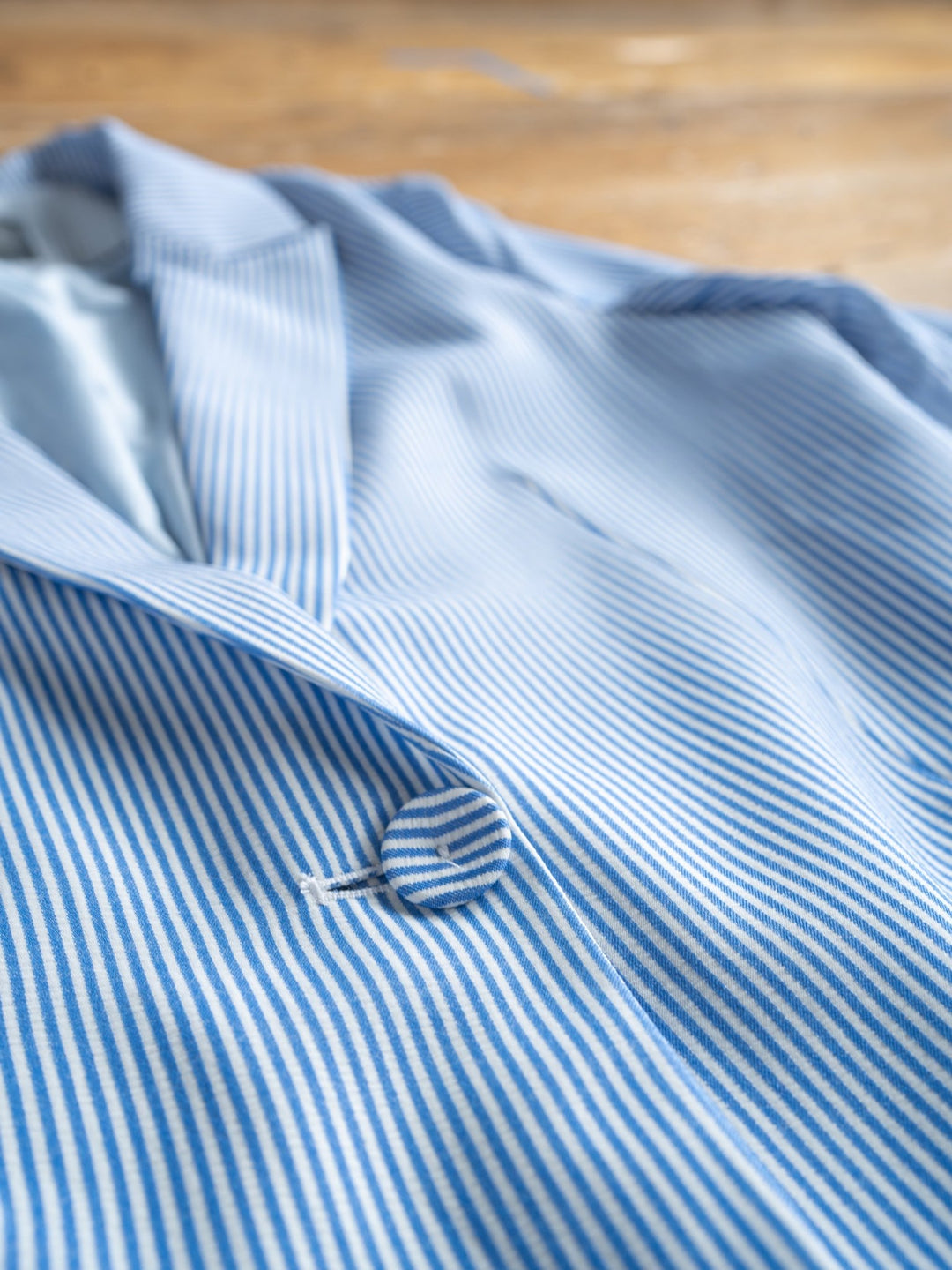 A close-up of The Malin {Set} by Savannah Sevens western life{&}style—a chic blue and white pinstripe blazer with notched lapel and single button fastening, laid flat on wood, part of a matching blazer and shorts set.