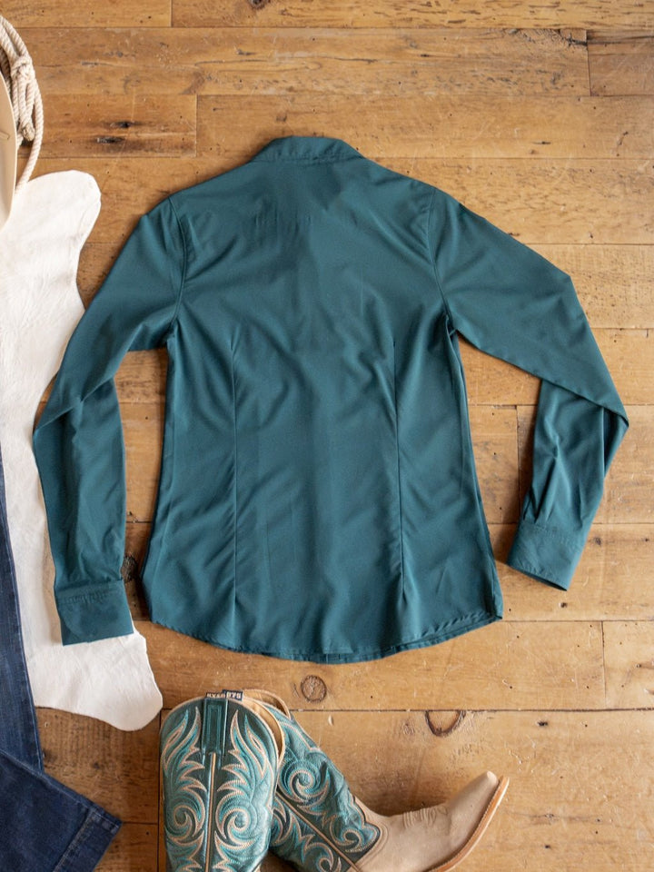 The Mankato Teal Mesh Performance Shirt by Savannah Sevens western life{&}style is laid flat on a wooden floor, accompanied by turquoise cowboy boots, with part of a white cowhide and denim jeans visible nearby.