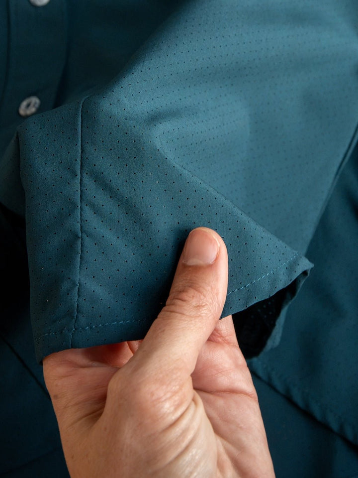 A hand holds the cuff of the Savannah Sevens western life{&}style Mankato Teal Mesh Performance Shirt, highlighting the textured, teal perforated fabric and small mesh holes in the material.