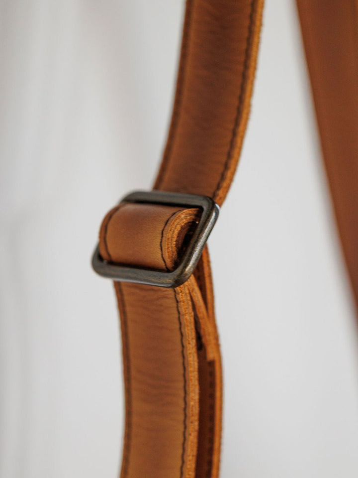 Close-up of a tan leather strap with visible stitching and rectangular metal buckle from the Maramec Leather Crossbody Handbag by Savannah Sevens western life{&}style, set against a plain light background. By STS.