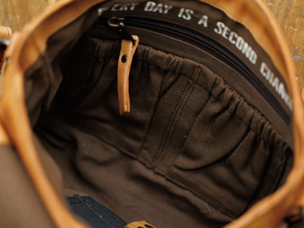 A close-up of the Maramec Leather Crossbody Handbag by Savannah Sevens western life{&}style shows several fabric pockets, a zippered compartment with a leather pull tab, and white-stitched lining that reads "EVERY DAY IS A SECOND CHANCE.