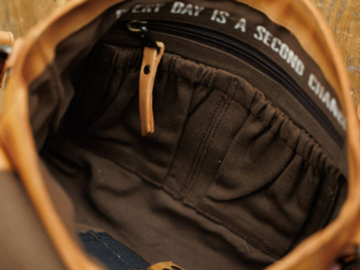 A close-up of the Maramec Leather Crossbody Handbag by Savannah Sevens western life{&}style shows several fabric pockets, a zippered compartment with a leather pull tab, and white-stitched lining that reads "EVERY DAY IS A SECOND CHANCE.