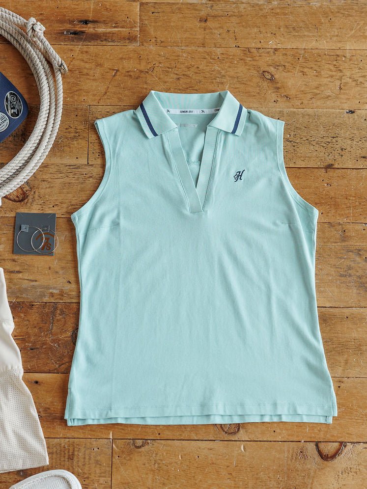 The Marengo sleeveless light blue collared golf top by Savannah Sevens western life{&}style, featuring dark blue trim and a small embroidered “H” on the chest, is displayed flat among nautical-themed items.
