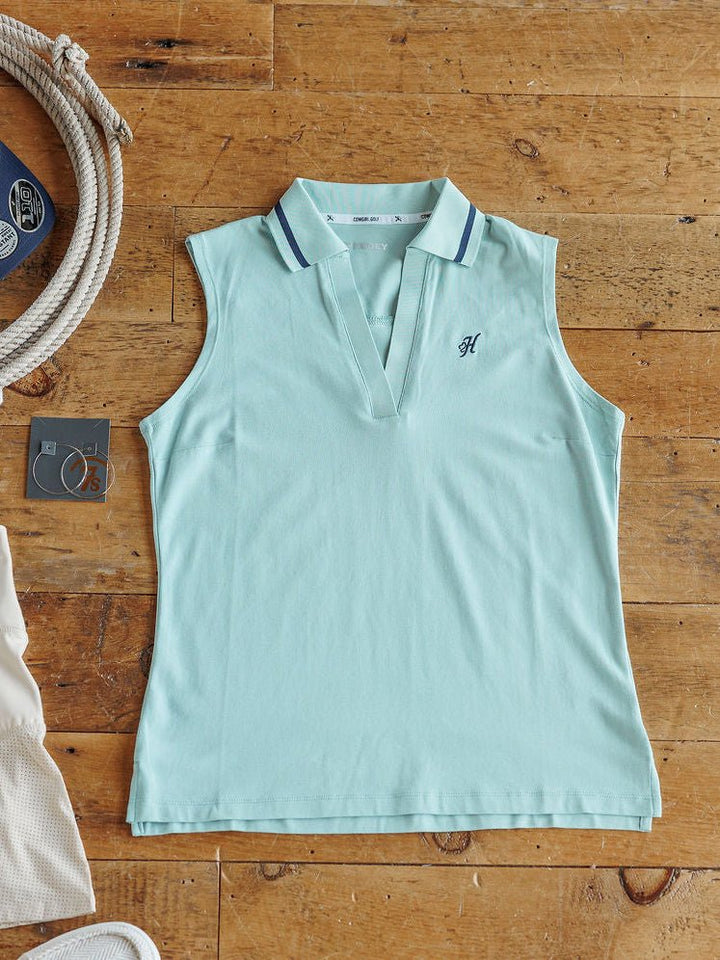 The Marengo sleeveless light blue collared golf top by Savannah Sevens western life{&}style, featuring dark blue trim and a small embroidered “H” on the chest, is displayed flat among nautical-themed items.