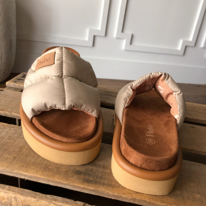 The Marfa {Natural} sandals by Savannah Sevens western life{&}style feature beige puffer straps, brown suede, cushioned insoles, and thick light tan shock-absorbing outsoles on a rustic wooden surface against a white paneled wall.