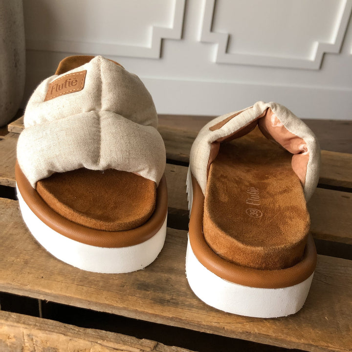 The Marfa {Oatmeal} platform sandals by Savannah Sevens western life{&}style feature cushioned insoles and white soles in beige and tan, displayed on wood against a white paneled wall.