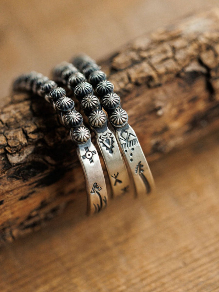 Three Marimar Cuff bracelets by Savannah Sevens western life{&}style rest on rustic wood. These sterling silver cuffs feature southwest-inspired engraved designs with geometric shapes, lines, and floral motifs.