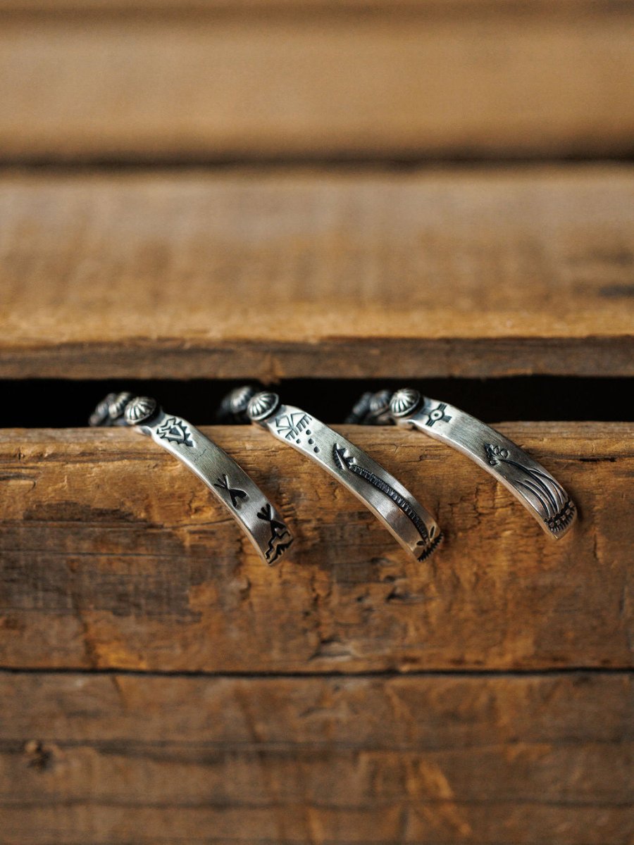 The Marimar Cuff by Savannah Sevens western life{&}style rests on a rustic wooden drawer, its engraved silver design highlighting southwest-inspired craftsmanship against a warm, earthy background.