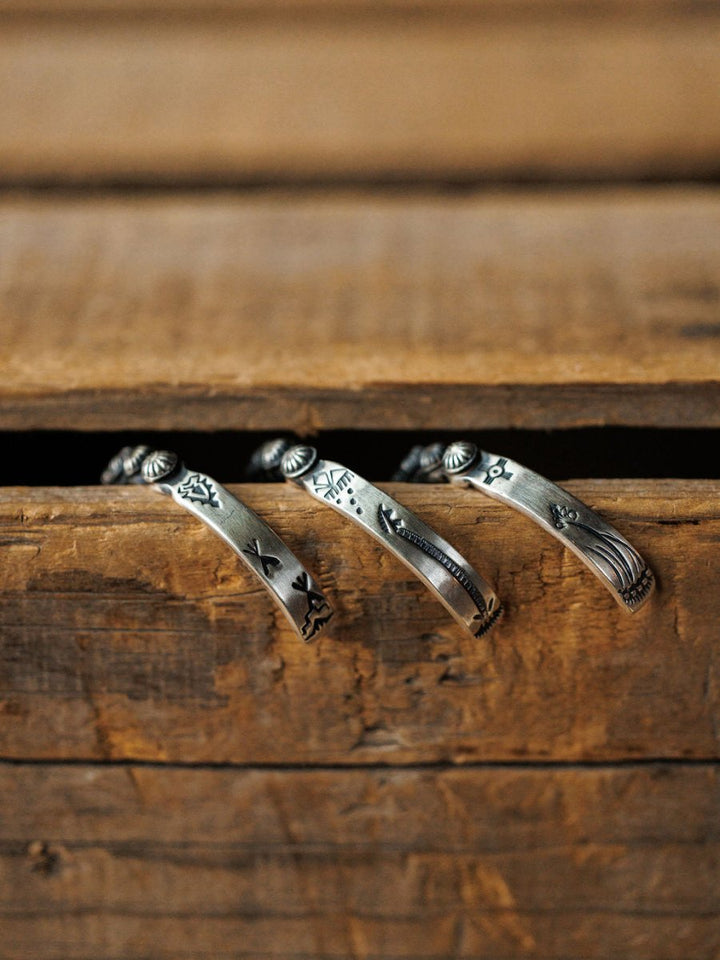 The Marimar Cuff by Savannah Sevens western life{&}style rests on a rustic wooden drawer, its engraved silver design highlighting southwest-inspired craftsmanship against a warm, earthy background.