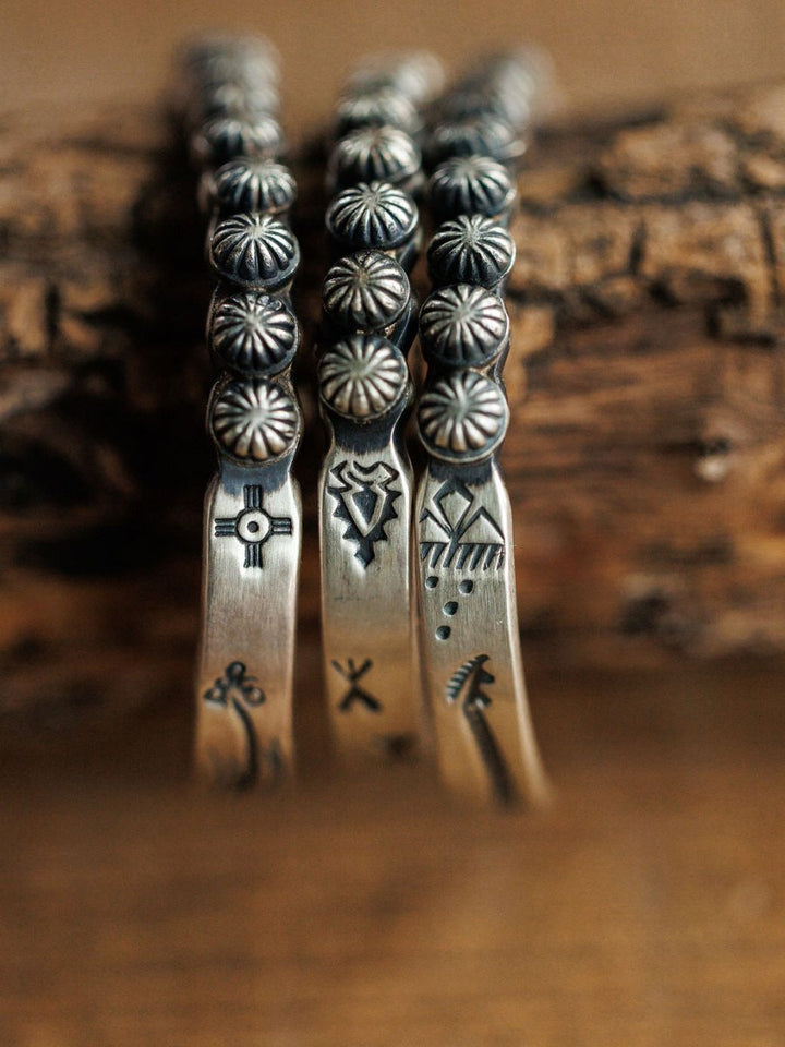Close-up of three Marimar Cuff bracelets by Savannah Sevens western life{&}style—handmade sterling silver with stamped geometric and symbolic motifs, raised details, and classic southwest style, displayed on rustic wood.