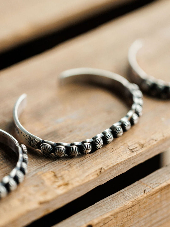 A close-up of the Marimar Cuff by Savannah Sevens western life{&}style, a handmade sterling silver bracelet with beaded designs, reflecting classic southwest style and displayed on rustic wood.