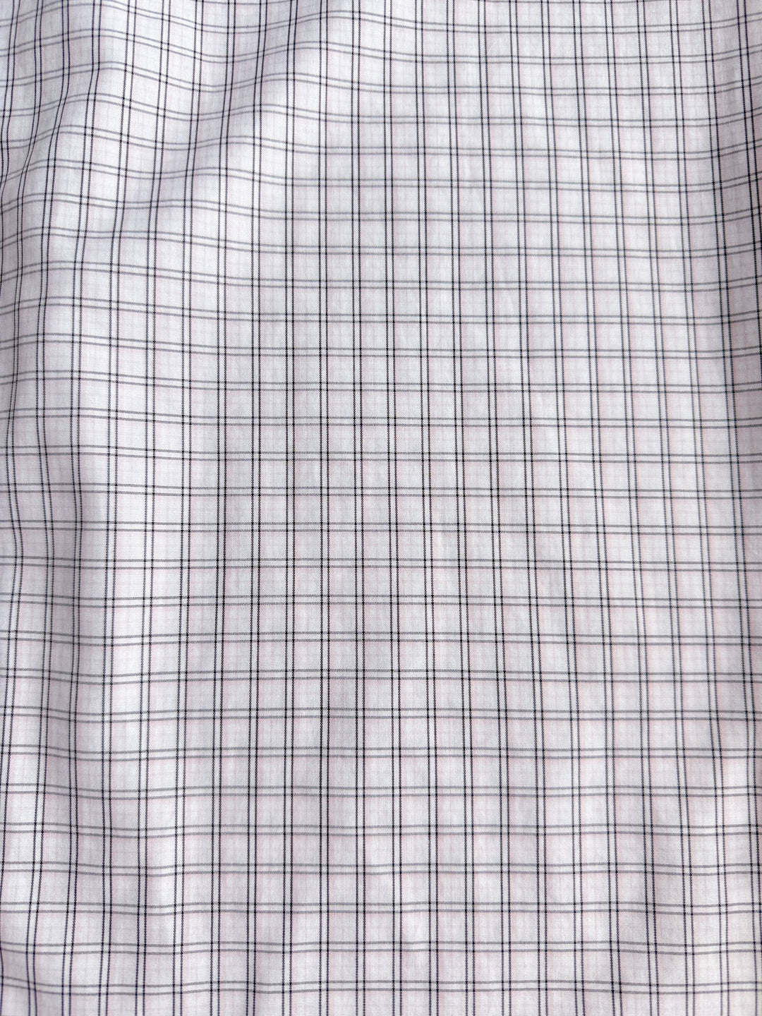 A close-up of the Marshall Ariat Men’s Plaid Button Up from Savannah Sevens western life{&}style showcases its white fabric with a grid pattern of thin black lines forming small squares. The slightly wrinkled material gives the plaid design a wavy appearance.