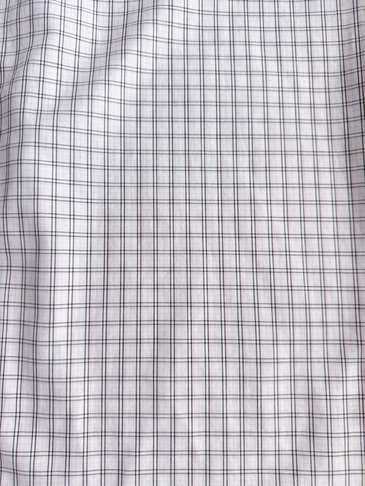 A close-up of the Marshall Ariat Men’s Plaid Button Up from Savannah Sevens western life{&}style showcases its white fabric with a grid pattern of thin black lines forming small squares. The slightly wrinkled material gives the plaid design a wavy appearance.