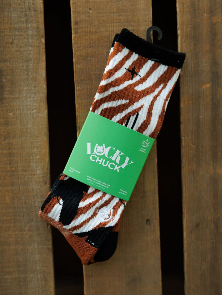 A pair of Maverick Crew Socks by Savannah Sevens western life{&}style, featuring brown, black, and white zebra stripes in an odor-fighting hemp blend, wrapped in a green Lucky Chuck label and displayed on a wooden surface.