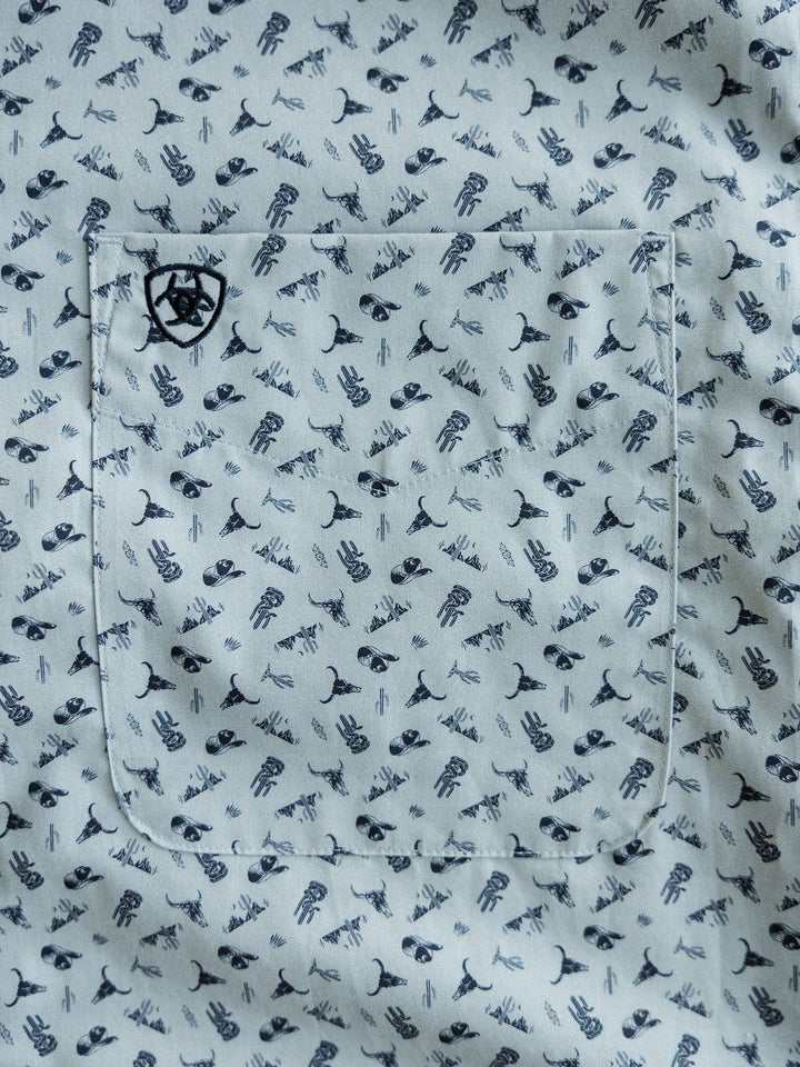 A close-up of the McGrath Ariat Men's Southwest Button Up by Savannah Sevens western life{&}style shows its pocket with a black geometric logo and a pattern of small cacti, whale tails, and eyes.