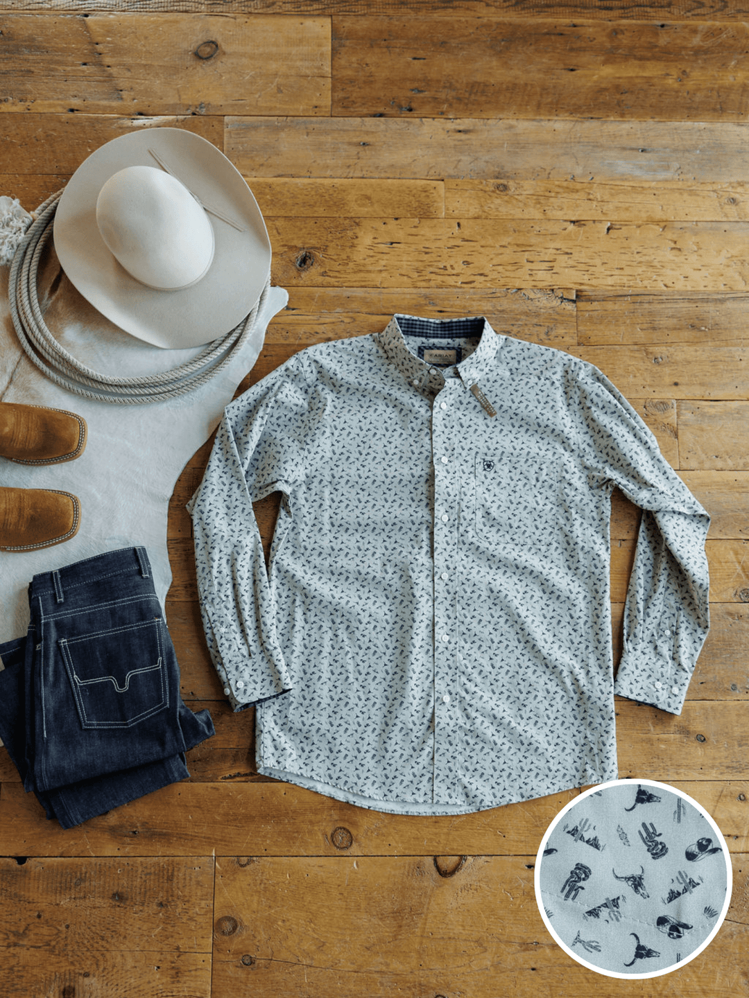 Flat lay of the McGrath Ariat Men's Southwest Button Up from Savannah Sevens western life{&}style, featuring a subtle bird and animal print, paired with dark jeans, brown shoes, a white cowboy hat, and rope on a wooden floor. Wrinkle-free for any occasion.