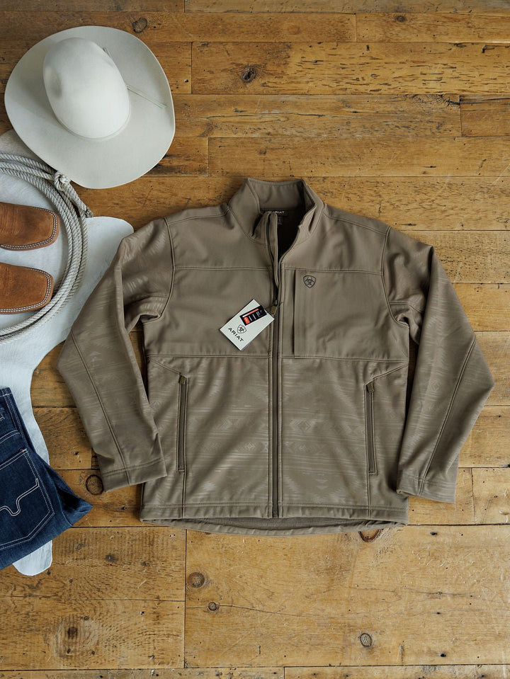 A McGregor Ariat Men's Southwest Insulated Jacket by Savannah Sevens western life{&}style is laid flat on a wooden floor with a white cowboy hat, coiled rope, tan boots, dark jeans, and a white cloth.