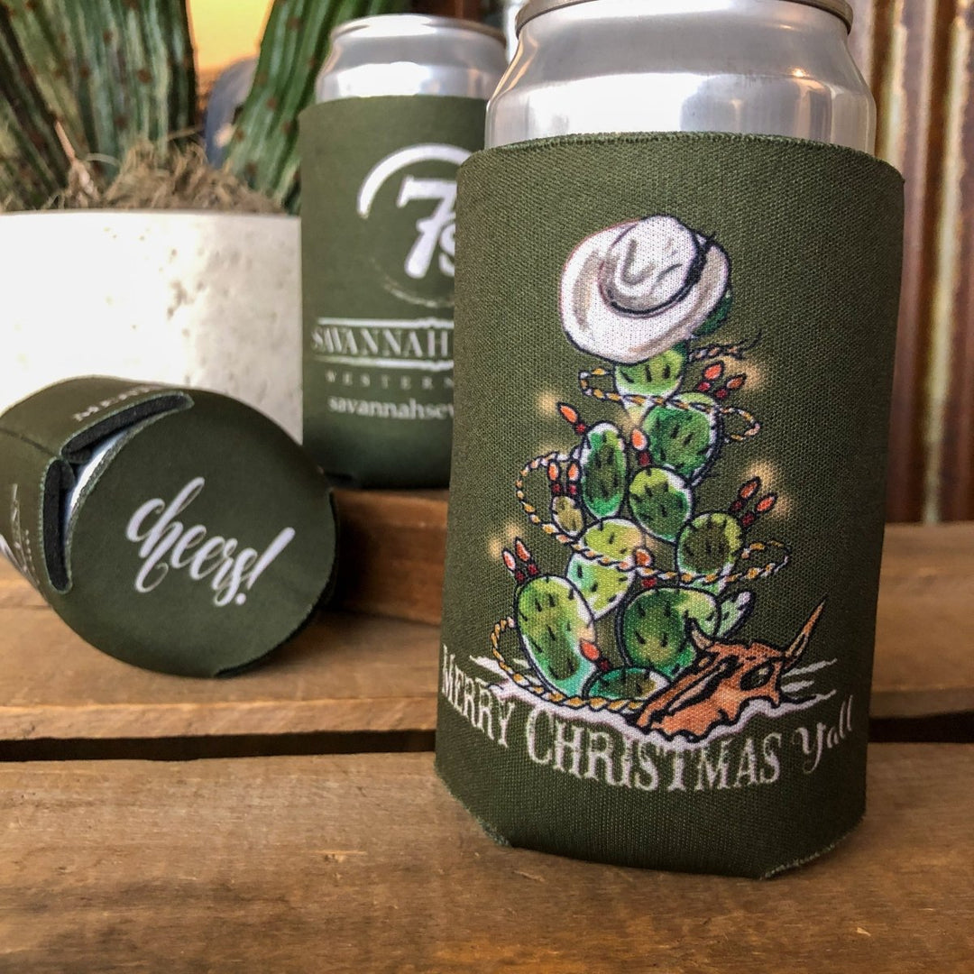 The Merry Christmas Y'all Koozie from Savannah Sevens western life{&}style features a festive cactus with ornaments, a cowboy hat, and steer skull, plus the text "Merry Christmas Y’all"—perfect for celebrating the season western style.