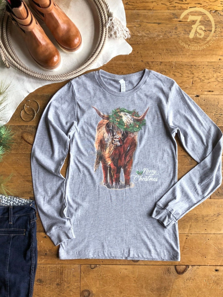 Merry Highland Graphic Tee: a grey long-sleeve women’s Christmas shirt featuring a Highland cow wearing a Christmas wreath with the text Merry Christmas beside it.