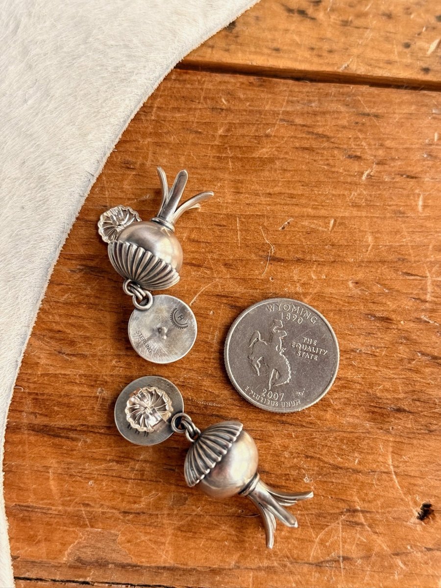 Mesa Earrings by Savannah Sevens western life{&}style—two sterling silver floral and pod-shaped earrings, handmade in the USA, are shown on a wooden surface beside a Wyoming state quarter for size; a white textured fabric appears on the left.