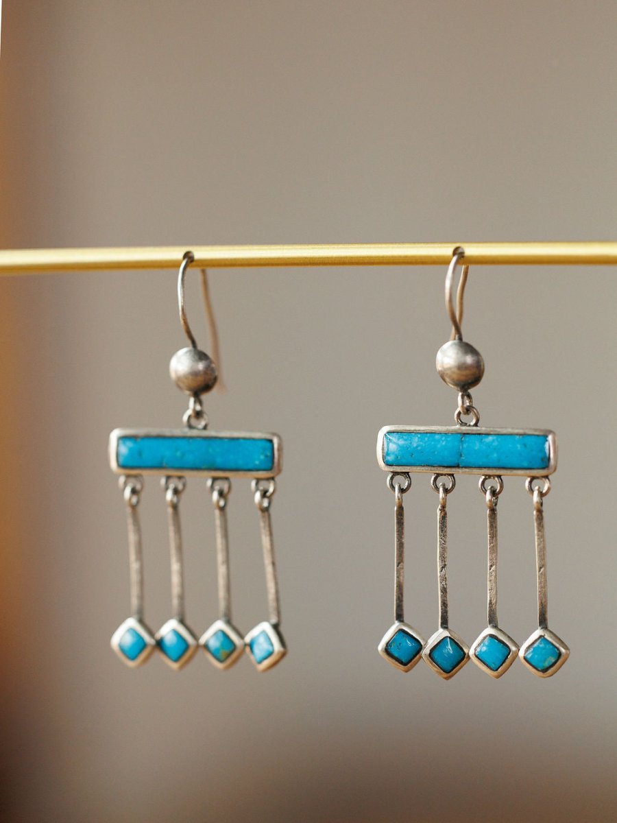 The Mesita Earrings by Savannah Sevens western life{&}style are handmade silver earrings, each featuring four rectangular Kingman turquoise stones, displayed on a horizontal rod with a soft blurred background.