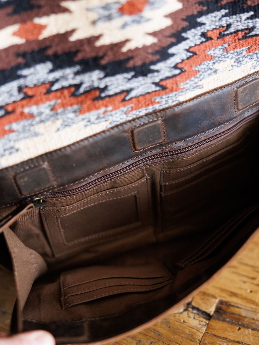 Close-up of the Mohave Backpack by Savannah Sevens western life{&}style, showing brown leather details, inner compartments, zipper pocket, and card slots on a wooden surface.