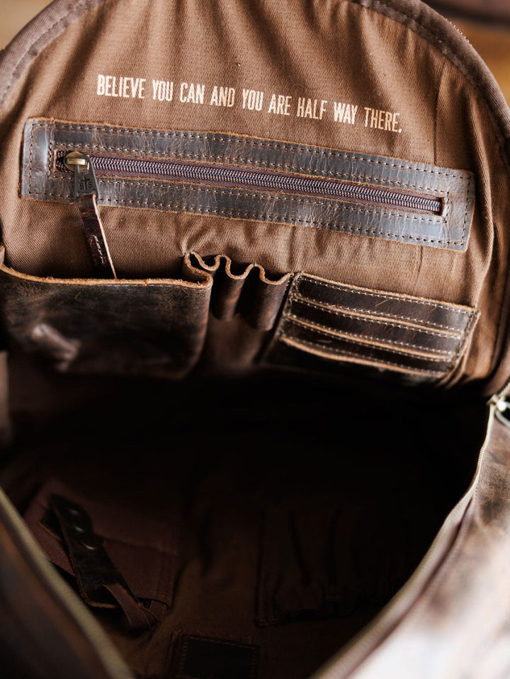 The Mohave Backpack by Savannah Sevens western life{&}style features an organized interior with pockets and a zipper compartment, plus the quote "BELIEVE YOU CAN AND YOU ARE HALF WAY THERE" printed on the inner flap. By STS. 